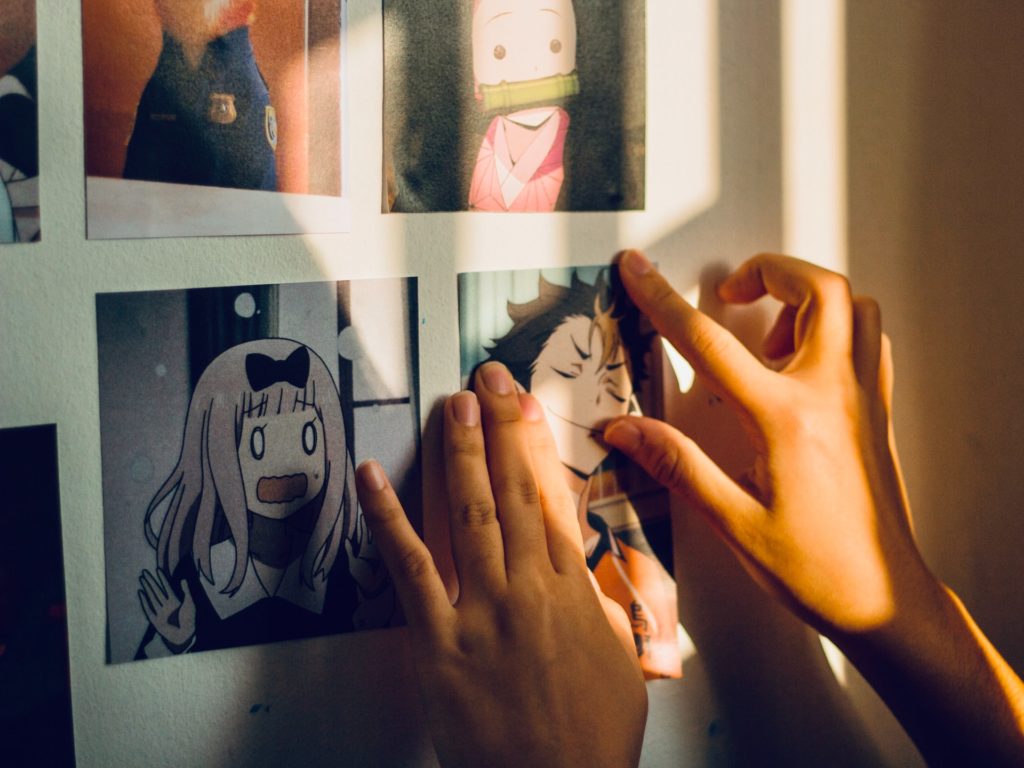 Duvara anime karakterlerinin resmini asan iki el,